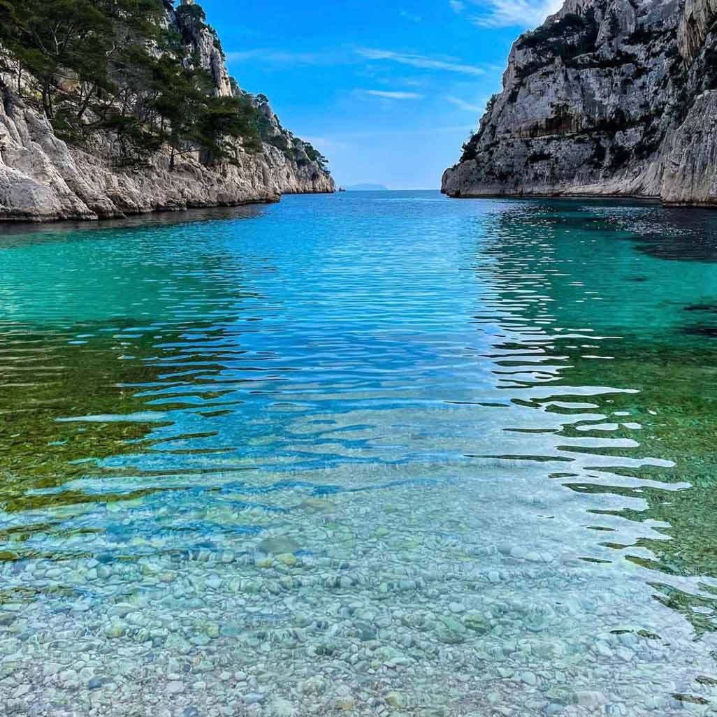 Eau cristalline et fond de galets blancs au bord du rivage de la calanque d'En-Vau.