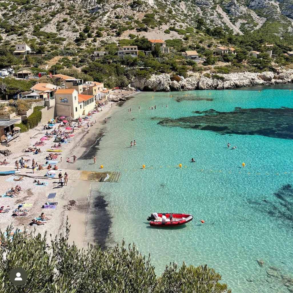 Plage de Sormiou animée bordée de cabanons traditionnels et d'eaux claires.