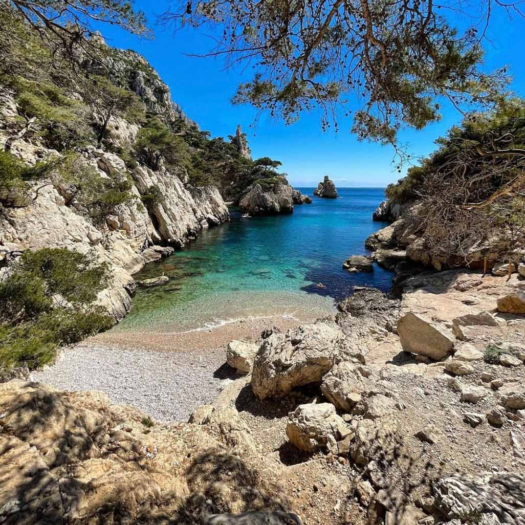 Plage de galets isolée et eaux turquoise cristallines de la calanque de Sugiton.