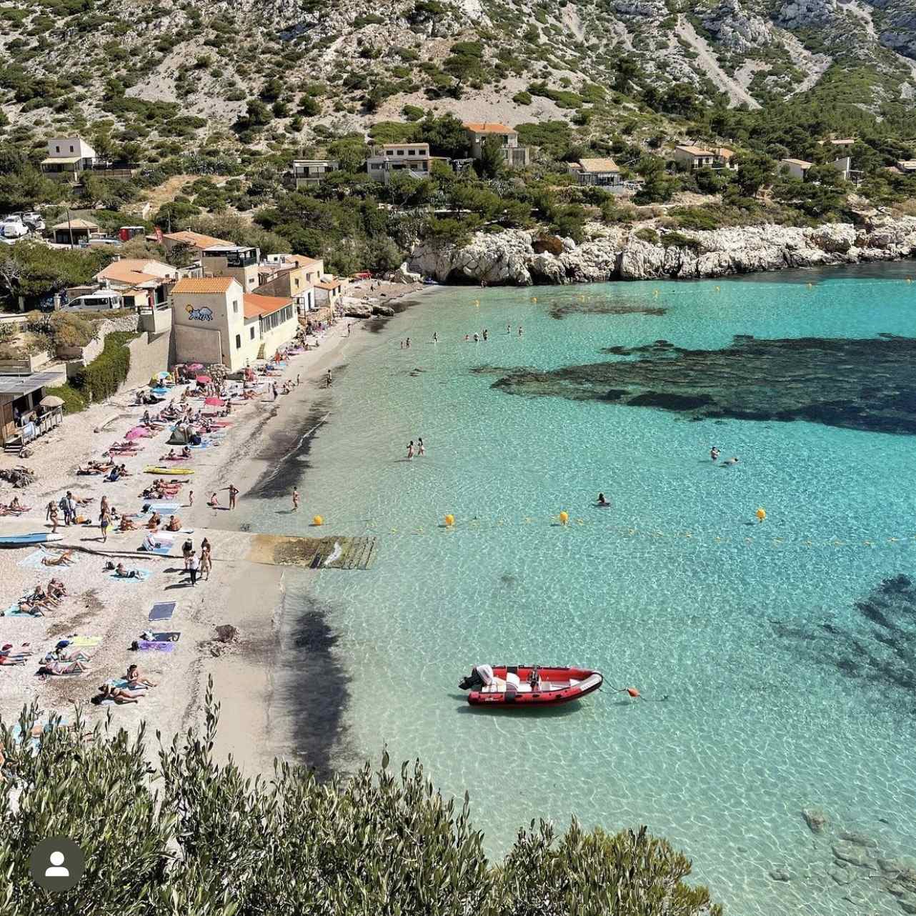 Vue aérienne plongeante sur la plage de galets, les cabanons traditionnels et les eaux turquoise et limpides de la calanque de Sormiou à Marseille.