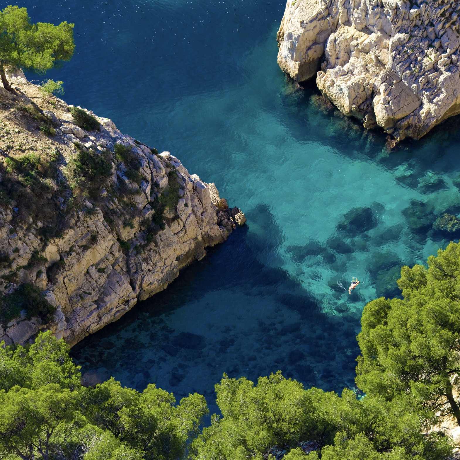 Un nageur dans les eaux turquoise au pied des falaises de Sugiton.